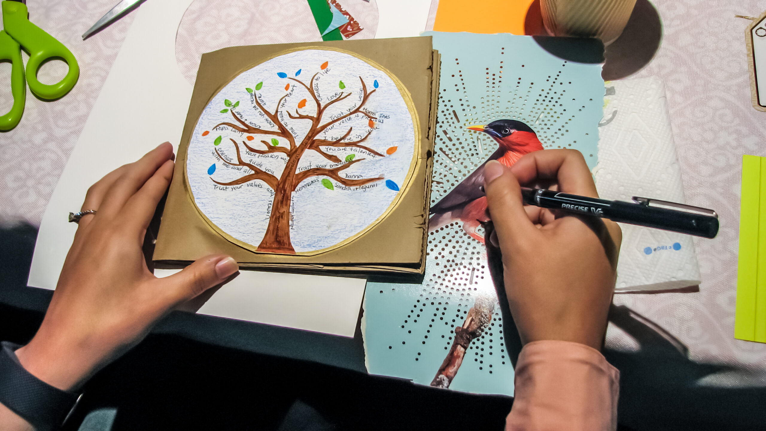 Hands creating a handmade art piece featuring a tree with messages, during a workshop inspired by Prodigal Daughter.